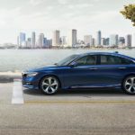 A blue 2020 Honda Accord is stopped at a stop sign in front of a river and city.