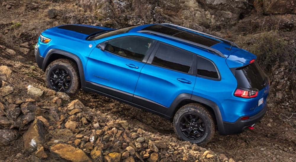 A blue 2020 Jeep Cherokee Trailhawk Elite is off-roading up a rocky trail, shown from the side.