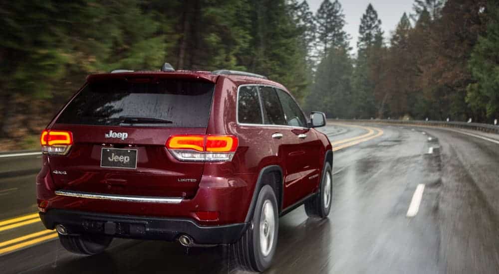 A red 2020 Jeep Grand Cherokee Limited is driving away on a road in the rain.