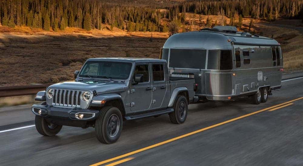 A gray 2020 Jeep Gladiator is towing an airstream trailer on a highway.