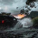 A silhouette of a 2020 Jeep Wrangler Unlimited is splashing through a river on a trail.