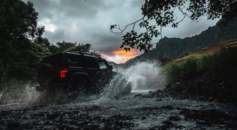 A silhouette of a 2020 Jeep Wrangler Unlimited is splashing through a river on a trail.