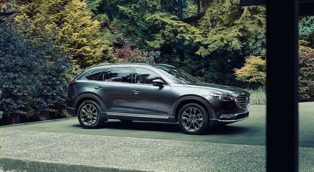 A gray 2020 Mazda CX-9 is parked in front of trees and shrubs.