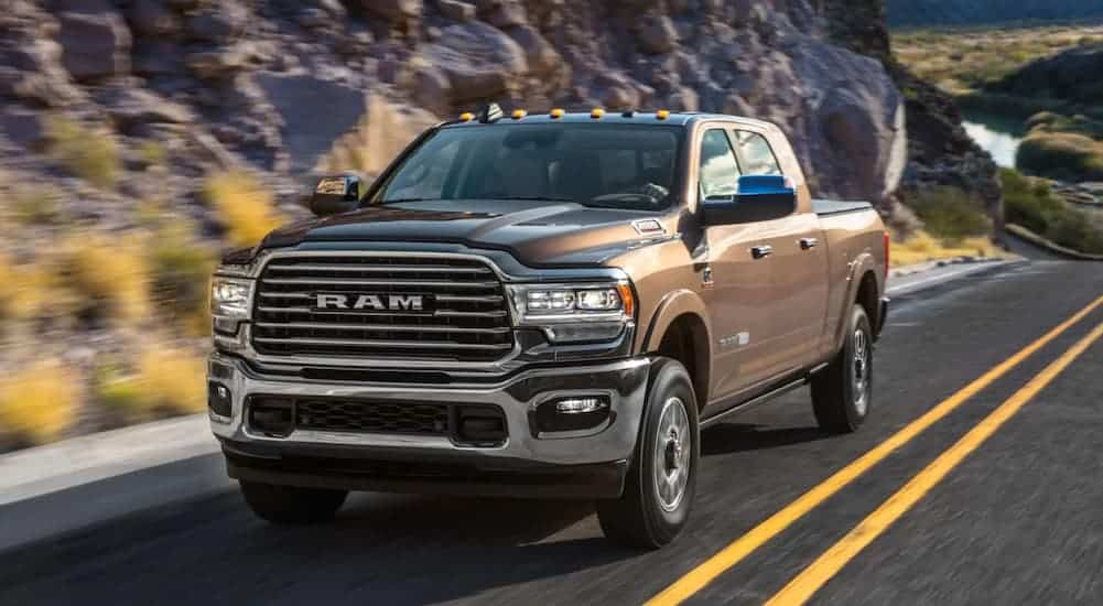 A brown 2020 Ram 2500 is driving uphill past rocky terrain.