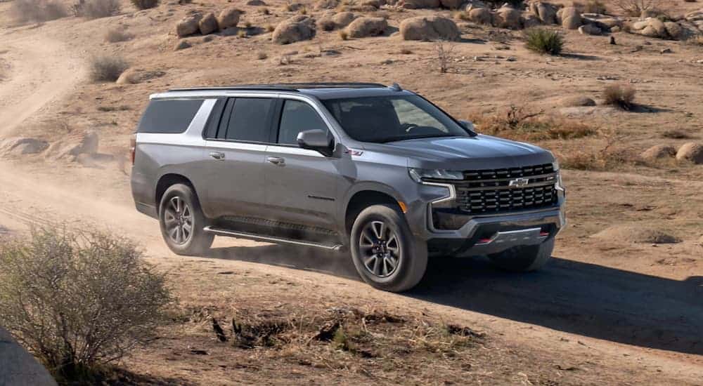 A grey 2021 Chevy Suburban is driving on a dirt road through the desert.