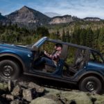 A blue 2021 Ford Bronco 4-door with no roof or doors is shown from the side climbing a mountain.