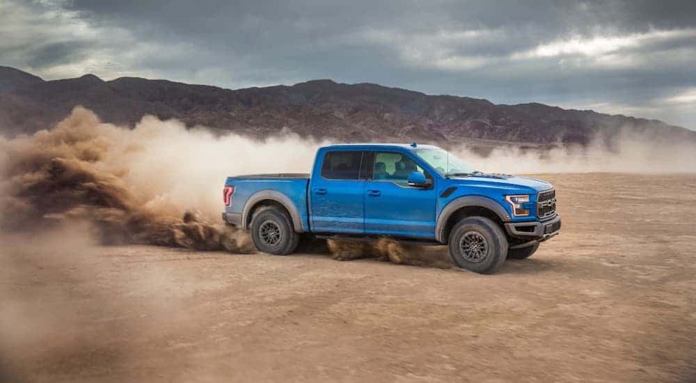 A blue 2020 Ford F-150 is kicking up dirt in a desert.