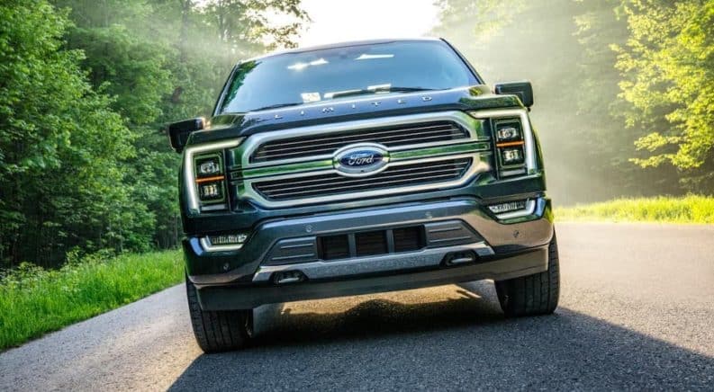 An angled photo shows the grille of a gray 2021 Ford F-150 Limited driving on a tree-lined road.
