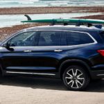 A blue 2021 Honda Pilot is parked at the beach with a surf board on top.