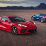 A red and a blue 2021 Chevy Corvette are parked on a flat field with mountains in the distance.
