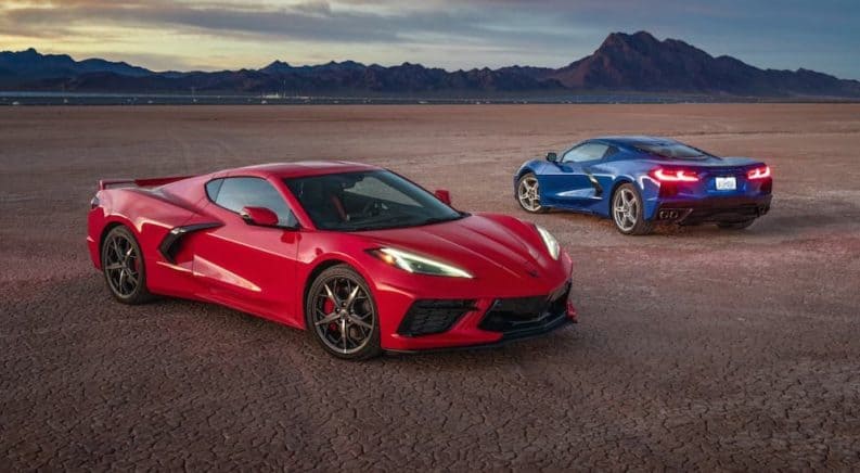 A red and a blue 2021 Chevy Corvette are parked on a flat field with mountains in the distance.