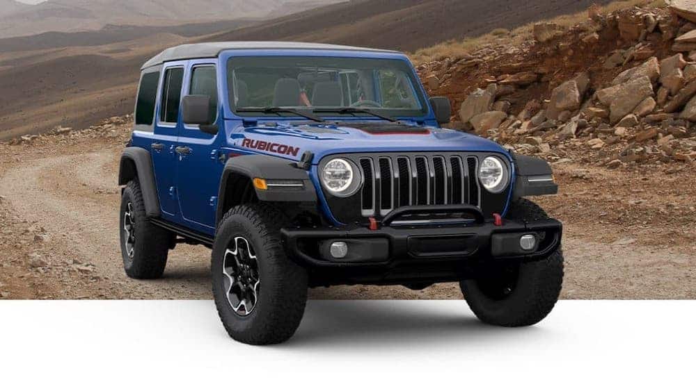 A blue 2020 Jeep Wrangler Rubicon Recon is driving on a dirt trail.