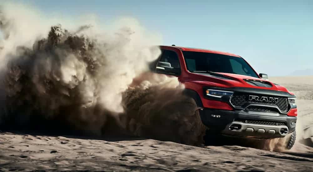 A red 2021 Ram TRX is off-roading in the sand kicking up a big dust cloud.