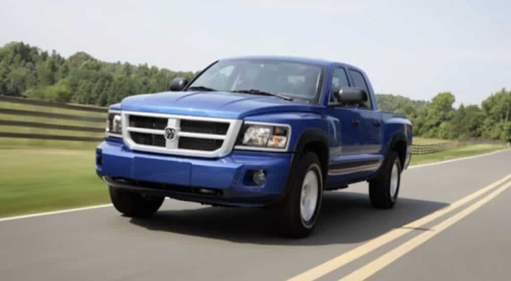 A blue 2008 Dodge Dakota is driving past a fenced in field.