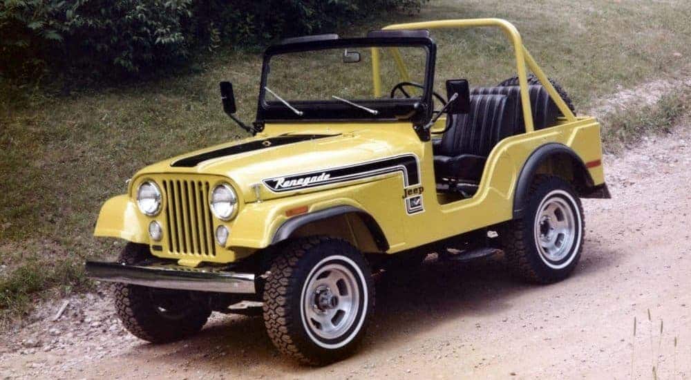 A yellow 1980s Jeep CJ-5 is parked on a dirt road.