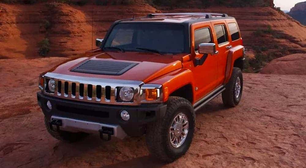 An orange 2008 Hummer H3 is parked in front of red rock formations.