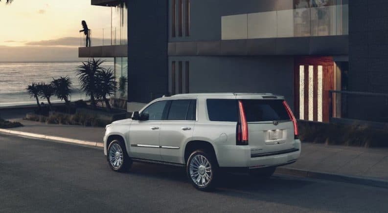 A popular used SUV for sale, a white 2018 Cadillac Escalade, is parked in front of a beach house at sunset.