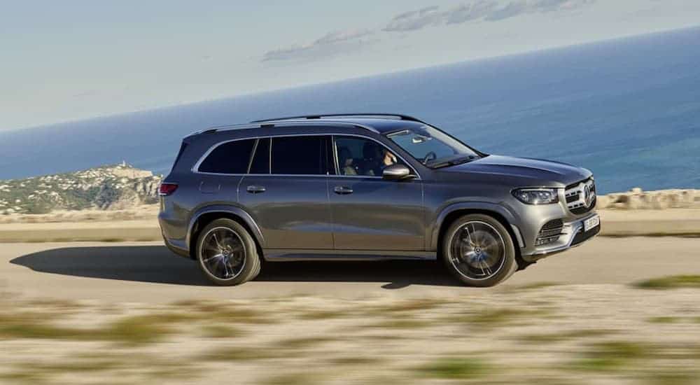 A gray 2019 Mercedes-Benz GLS is driving along a coastal road and shown from the side..