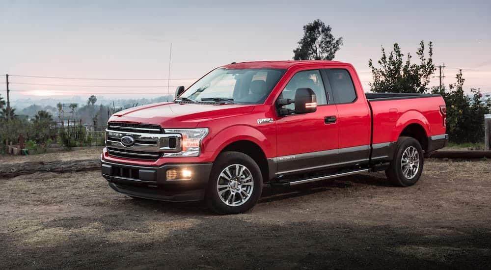 A red 2018 Ford F-150 is parked on dirt in front of trees and a power line.