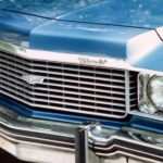 A blue 1974 Chevrolet Impala is showing a close up of the chevy emblem at a Chevy dealership.