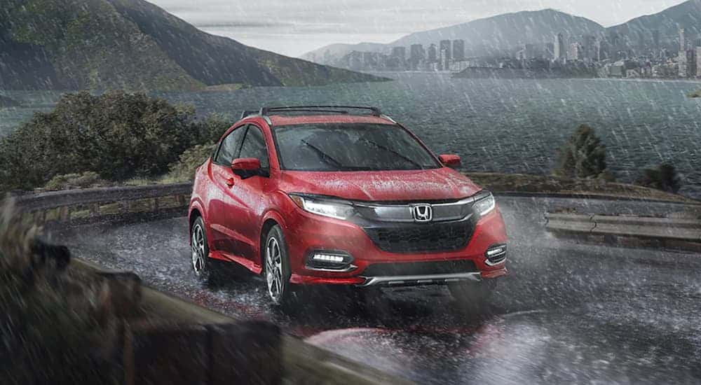 A red 2020 Honda HR-V is driving around a corner past a lake in the rain.