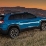 2020 Jeep Cherokee Trailhawk Elite is parked on grass overlooking mountains at sunset.