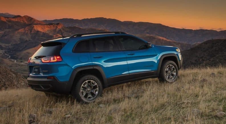 2020 Jeep Cherokee Trailhawk Elite is parked on grass overlooking mountains at sunset.