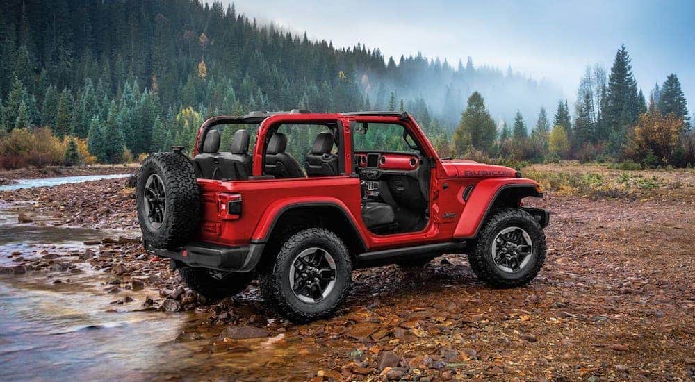A red 2020 Jeep Wrangler with no roof or doors is next to a woodland river as part of the 2020 Jeep Wrangler vs 2020 Jeep Gladiator comparison.