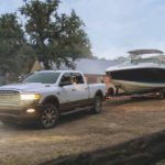A white 2020 Ram 2500 is towing a boat on a farm.
