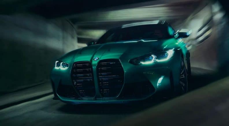 A green 2021 BMW M3 is driving through a parking garage with its daytime running lights on.