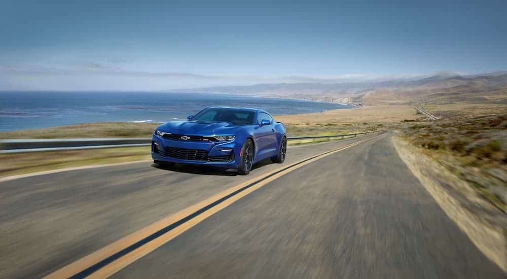 A blue 2021 Chevrolet Camaro SS is driving down a road with the ocean in the background.