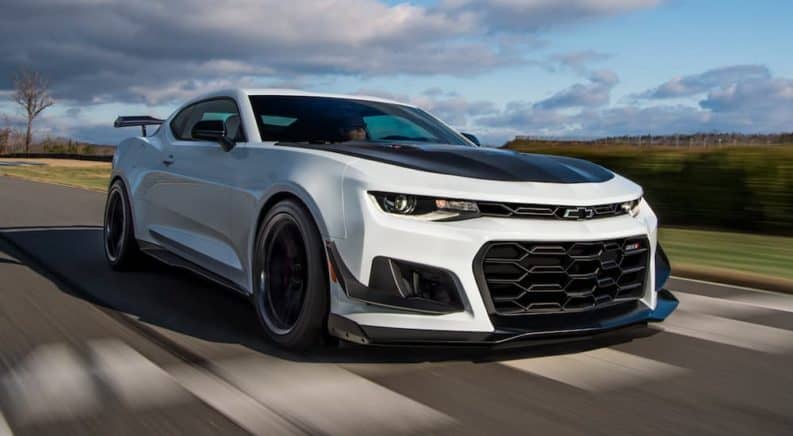 A white 2021 Chevy Camaro with black accents is driving past a blurry field.