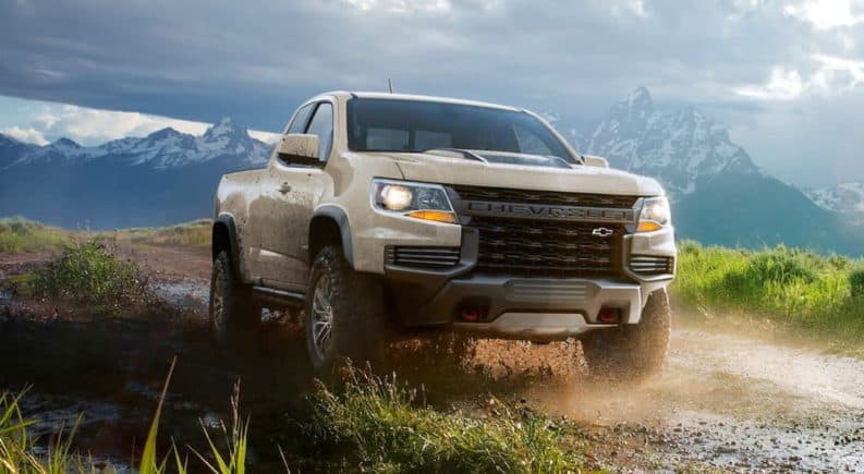 A tan 2021 Chevy Colorado ZR2 is driving on a dirt path in front of mountains.