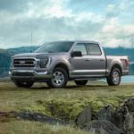 A grey 2021 Ford F-150 is parked on grass in front of a lake and mountains after winning the 2021 Ford F-150 vs 2020 Ford F-150 comparison.