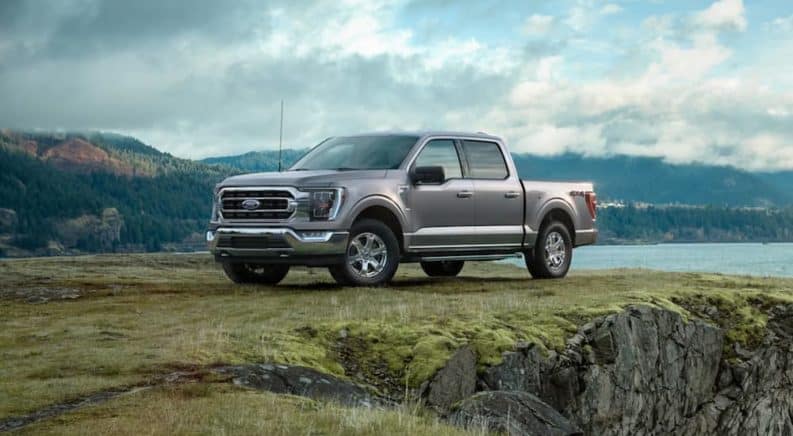 A grey 2021 Ford F-150 is parked on grass in front of a lake and mountains after winning the 2021 Ford F-150 vs 2020 Ford F-150 comparison.