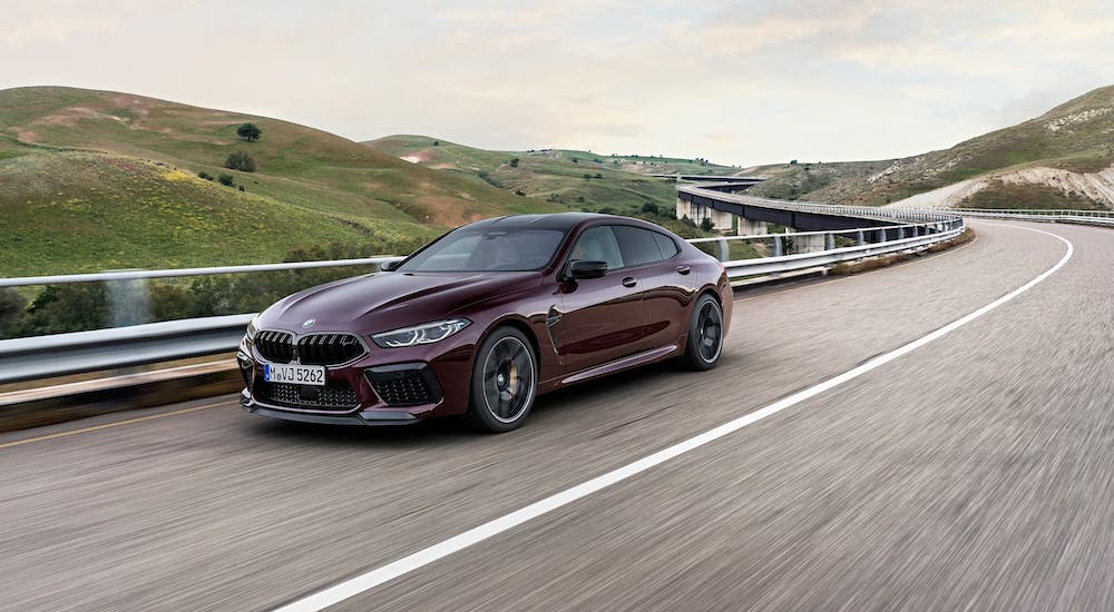 A burgundy 2020 BMW M8 Gran Coupe is driving on a highway.