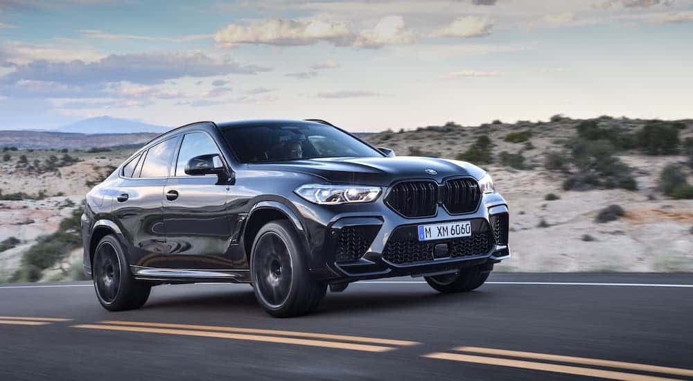 A black 2020 BMW X6 M Competition is driving on a desert highway.