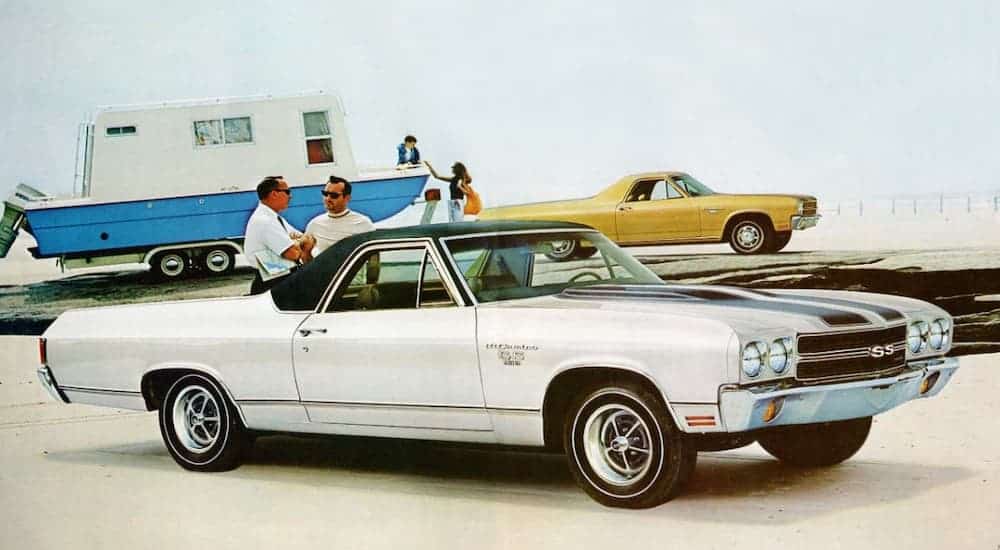 A white 1970 Chevy El Camino SS is parked in from of a yellow El Camino towing a boat.