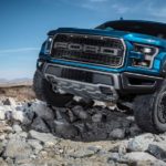 A blue 2020 Ford Raptor, a popular Ford truck for sale, is off-roading on rocks.