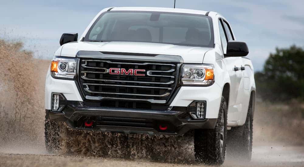 A white 2021 GMC Canyon AT4 is off-roading in mud after leaving a GMC dealer.