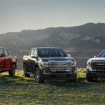 A red, a black, and a white 2021 GMC Canyon are parked on grass in front of mountains.