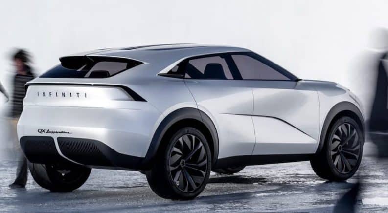 A profile view of a white Infiniti QX Inspiration concept car shows it parked with blurred images of people around it.