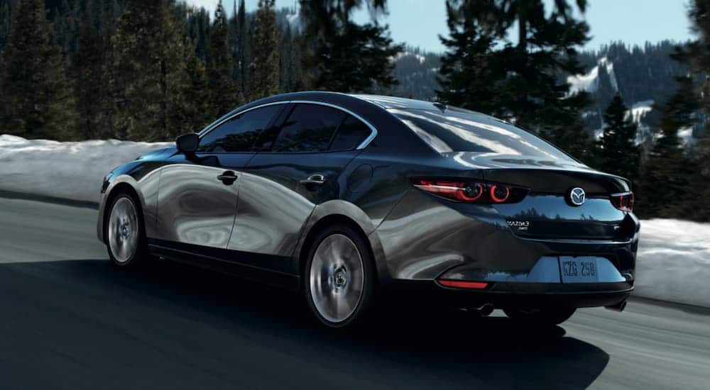 A grey 2021 Mazda 3 is driving on a snow-lined road after leaving a Mazda dealer.