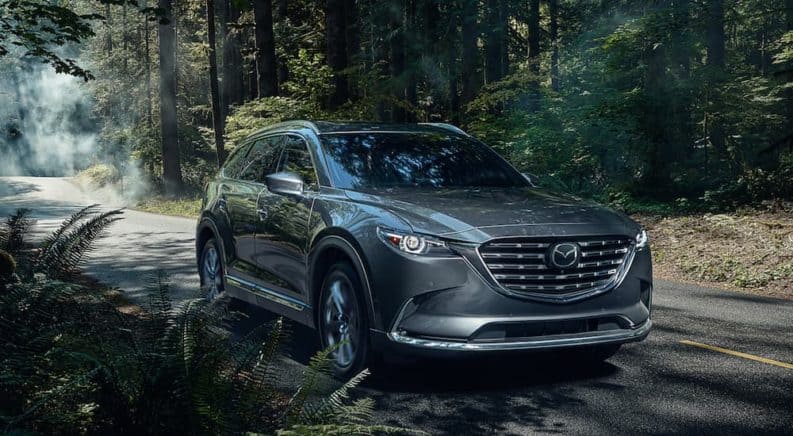 A grey 2021 Mazda CX-9 is driving on a road through the woods.