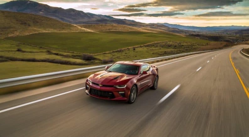 A red 2017 Chevy Camaro SS is driving on a rural highway.