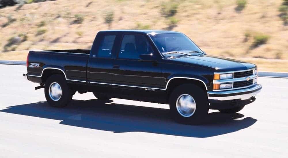 A black 1999 used Chevy Silverado is driving past dry grass and shrubs.