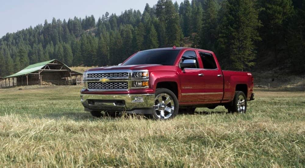 A red 2015 used Chevy Silverado is parked in a field in front of a small barn.