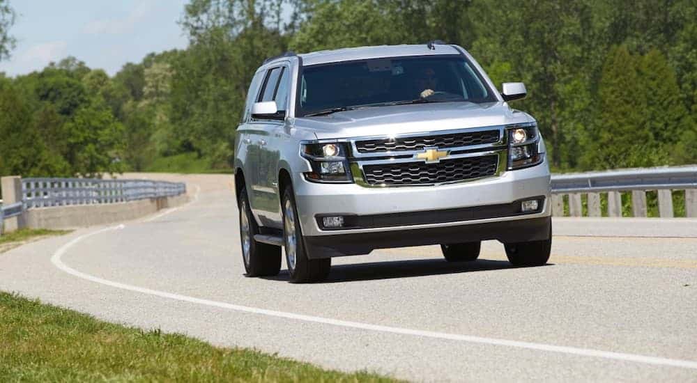 A silver 2015 used Chevy Tahoe LT is driving on a winding road.