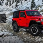 A red 2018 used Jeep Wrangler is parked in front of a grey Unlimited on a snowy mountain trail.