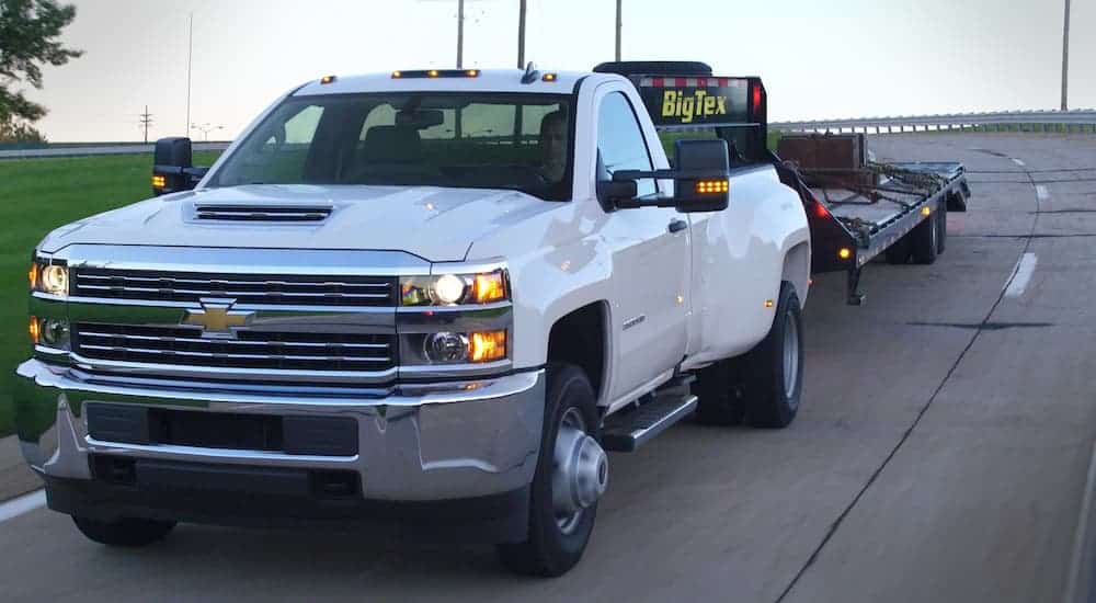 A white 2016 Chevrolet Silverado is towing a large trailer down the highway.